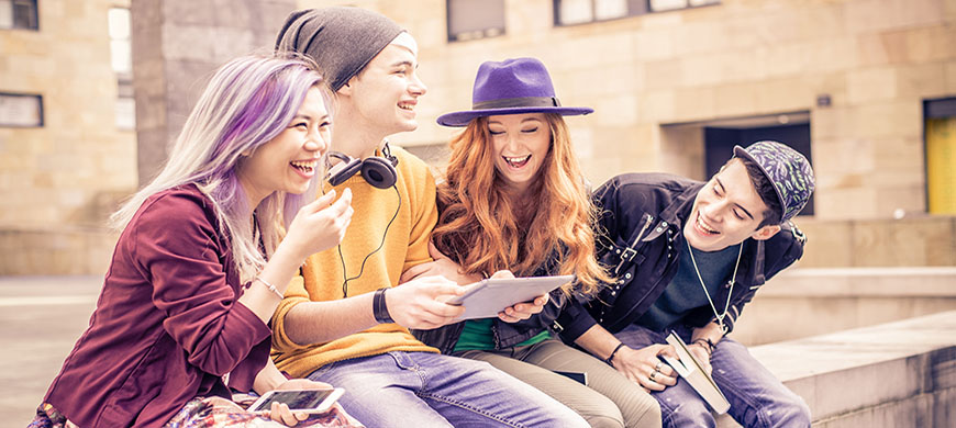 Multiracial group of best friends laughing and having fun outdoors - Multiethnic young teenagers looking down at computer tablet